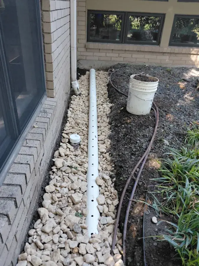 Drain pipe and stone visible in an open trench beside a home