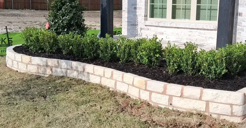 Shrubs and dark mulch inside a curved light stone bed border